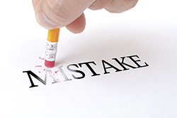 Male hand holding wooden pencil and delete word "MISTAKE" on the white paper